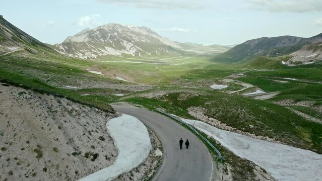 Two person are walking on tarmac curvy mountains road. On a beautiful sunny day. In the Italian mountains of Gran Sasso in the Abruzzo region.