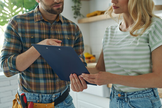 Close-up of confident handyman holding clipboard while woman signing documents