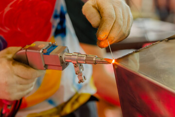 Close up: welder hands using portable handheld laser welding machine. Manufacturing, industrial,...
