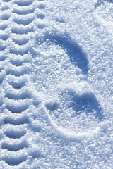 A winter road with shoe footprints, tracks wheel tire tread on white blue fluffy snow background....