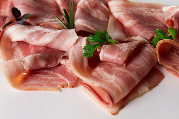 Raw bacon, sliced, with micro greenery and spices, on a white background, close-up,