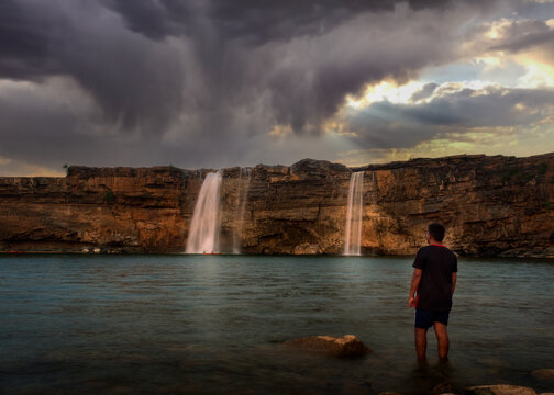 Man standing facing a waterfall