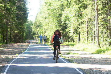 A woman rides a bicycle, in the summer in the park on a bike path.