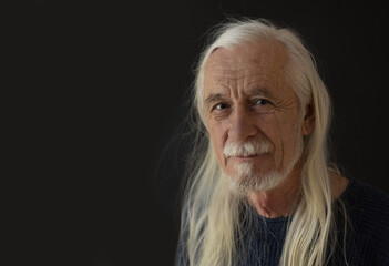 Low key studio  portrait of smiling attractive old man with loose long gray hair. Horizontally. 