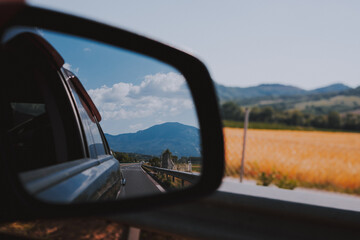 Fototapeta premium Car rear view mirror. Road, field and mountain reflection in mirror. Traveling in Europe