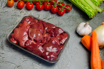 Raw chicken liver, vegetables and spices for making pate on a textured concrete-gray background.