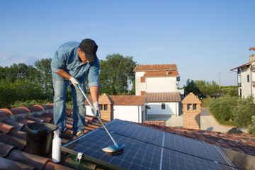 Image of a man on the roof of a house who cleans the solar panels with a mop for maximum efficiency. Ordinary maintenance work