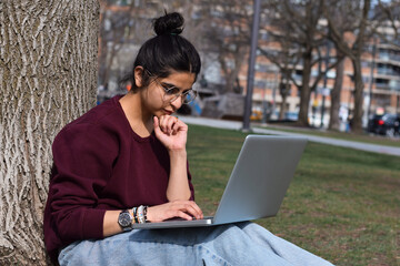 Young girl student sitting under tree in park using laptop computer