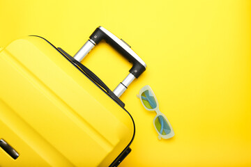 yellow suitcase and blue sunglasses on a yellow background. Top view, summer concept