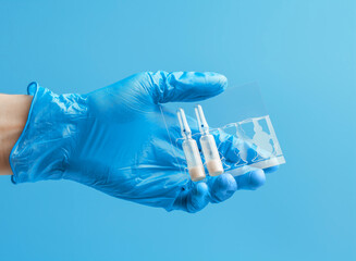Medical glove. Ampoules with a white liquid in the hand in a blue medical glove. Isolated on a blue background.