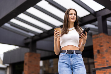 Portrait of young woman drinking coffee takeaway and talking on mobile phone while walking at city street