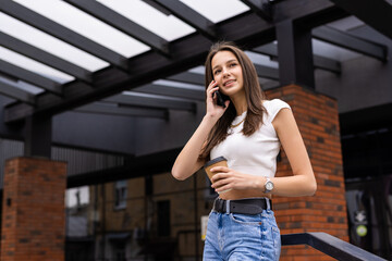 Fototapeta premium Successful female manager in elegant wear walking on city street and talking on mobile
