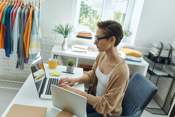 Confident young woman using laptop while working in fashion store office