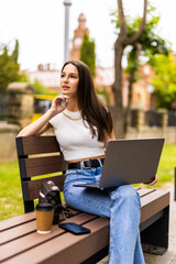 Young woman using a laptop on a bench in park