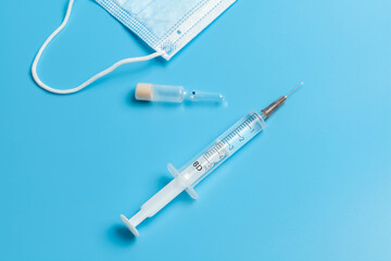Medical mask, syringe and ampoule. A blue medical mask with a white elastic band, a syringe and an ampoule isolated on a blue background.