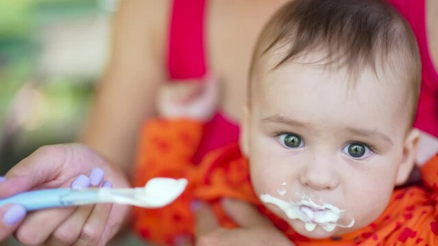 Adorable Caucasian child being given dairy food from spoon. Kid is full and pushes mom's hand away and stretches arms.