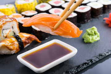 close-up, on a dark table, against the background of classic Japanese rolls, wooden sticks dip salmon sushi in soy sauce
