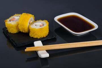 close-up, on a black table with a reflection, Japanese rolls with cream cheese and salmon in tempura, next to a container with soy sauce and wooden sticks