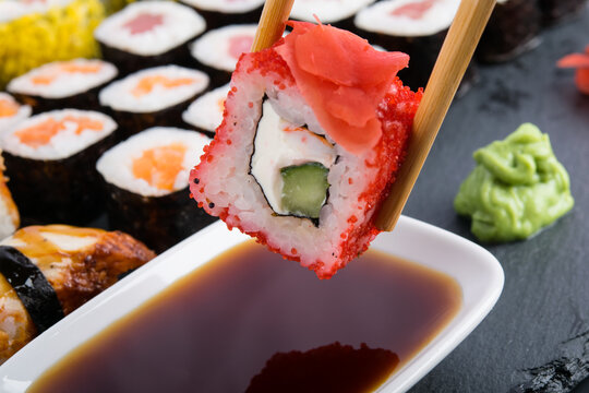 close-up, a roll with flying fish caviar with cucumber, ginger and cheese, lowered on wooden sticks into a container with soy sauce