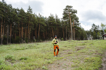 A man in tourist clothes stands against the background of the forest, a man in orange pants travels through the taiga area, trekking in nature, a hipster guy