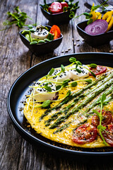 Tasty breakfast. Omelette  with green asparagus, goat cheese, pepper and cherry tomatoes served on black plate on wooden table
