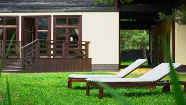 Lounge chairs on the backyard near the pond in a beautiful garden. Two empty sunbeds on the grass. Concepts of recreation, tanning in yard. Defocused foreground.