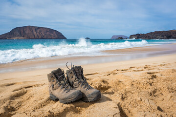 hiking boots on sand beach with ocean waves at Playa de las Conchas