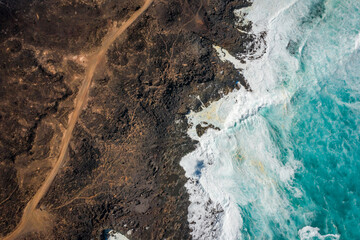 aerial view of hiking trail and ocean waves breaking on rocky coast 