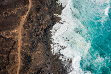 Obraz premium aerial view of hiking trail and ocean waves breaking on rocky coast 