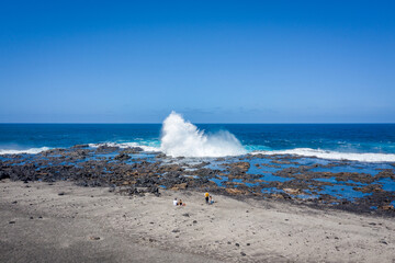 high ocean wave breaking on coastal rocks and stones with people watching at tenesera lanzarote