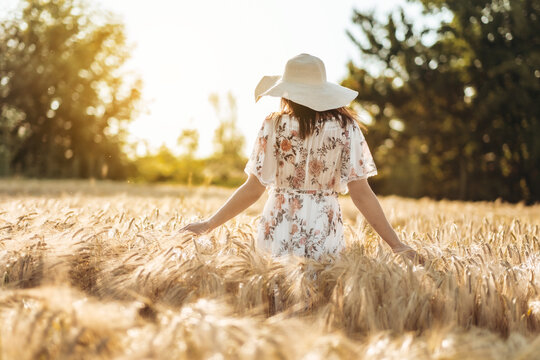 a woman in a sundress walks through a wheat field at sunset