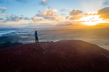 Fototapeta premium man standing on volcano enyoing lanzarote landscape during sunrise 