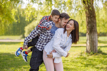 Fototapeta premium Portrait of happy Caucasian family in green summer park. Parents with son hugging in live.