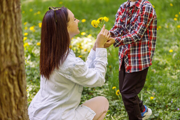 Obraz premium Beautiful young mother getting flowers from small son in park. Woman with dandelions from kid.