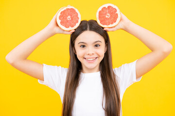 Happy teenager portrait. Teenage girl holding a grapefruit on a yellow background. Smiling girl.