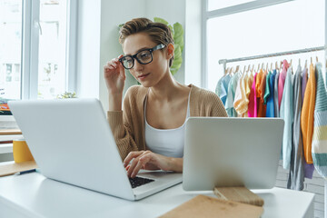 Confident young woman using laptop while working in fashion store office