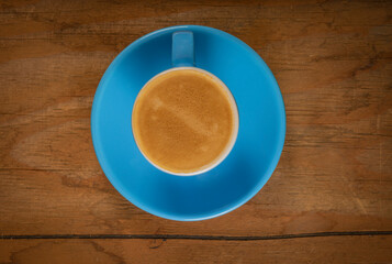Fresh coffee in blue cup on dirty old wooden table from above