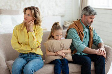 Unhappy Middle Aged Parents And Little Daughter Sitting At Home