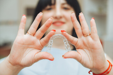 A beautiful smiling woman holds invisible aligners in her hands to align teeth for orthodontic...