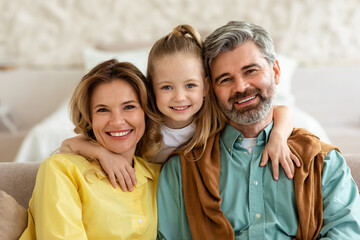 Parents And Little Daughter Smiling To Camera Embracing At Home