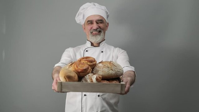 Professional baker offering freshly baked bread. Chef-cooker in a chef's hat and jacket. Senior baker man wearing a chef's outfit. Character kitchener, pastry chef for advertising.