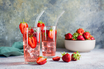 Refreshing cocktail with strawberries in glasses with a straw on the table and a bowl with berries.