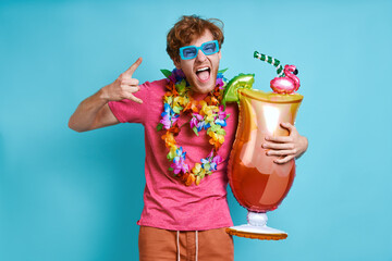 Playful redhead man carrying cocktail shaped balloon and gesturing against blue background
