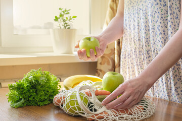Woman disassembles a knitted bag with groceries after shopping. A woman takes green apples out of a...