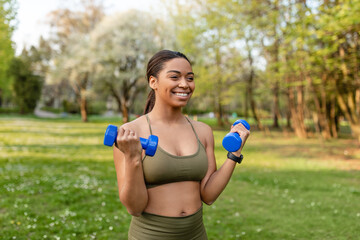 Outdoor sports concept. Strong young black woman exercising with dumbbells at city park, copy space