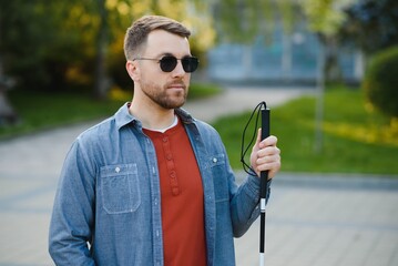 Young handsome blinded man walking with stick in town