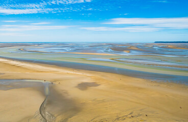 Fototapeta na wymiar Tourists walking on the colourful sand flats surrounding Le Mont Saint Michel during low tide, Normandy, Northern France 