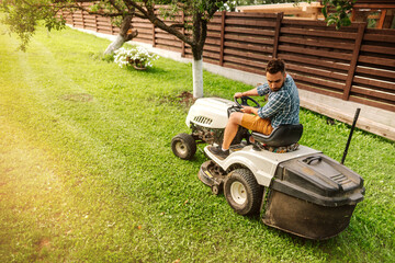 Industrial handsome worker using ride-on tractor, lawn tractor. Lawn mowing details with tractor...