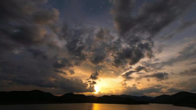 Timelapse video of sunset sky with rain and storm clouds above mountains and dam within twilight time. 