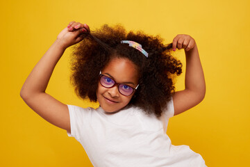 portrait of a young African girl in glasses smiling and rejoicing on a clean yellow background
